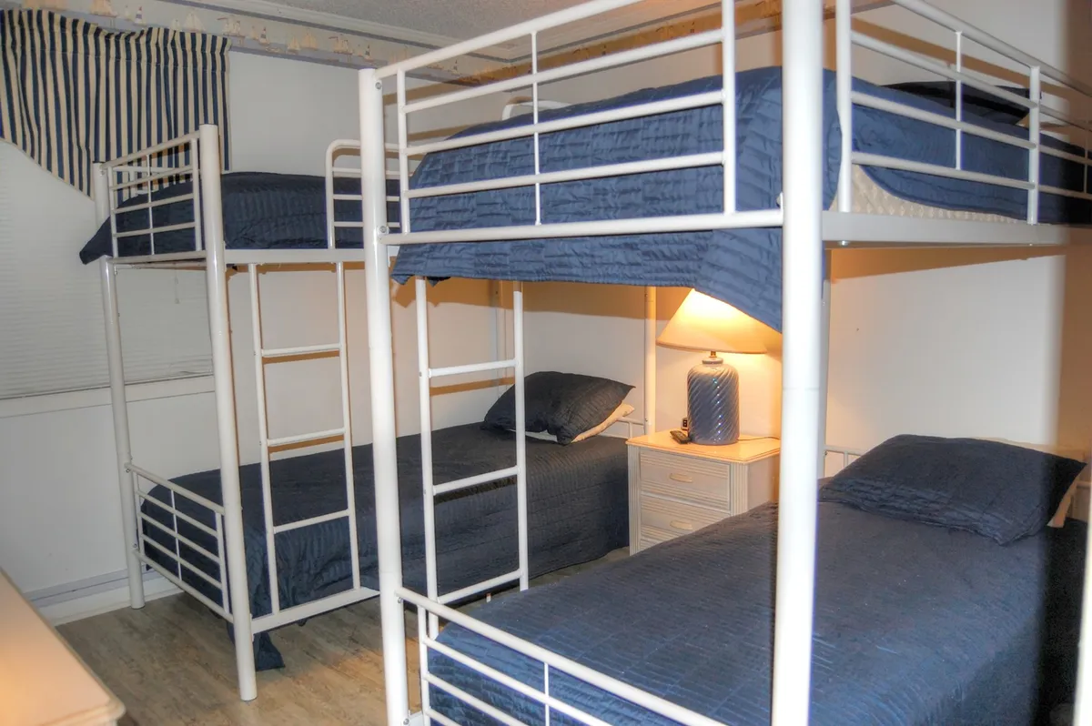 A cheerful bunk room with sturdy bunk beds, crisp bed linens, a nightstand, and a lamp. The playful arrangement and inviting setup make it ideal for children or friends, encouraging late-night chats and cozy relaxation.