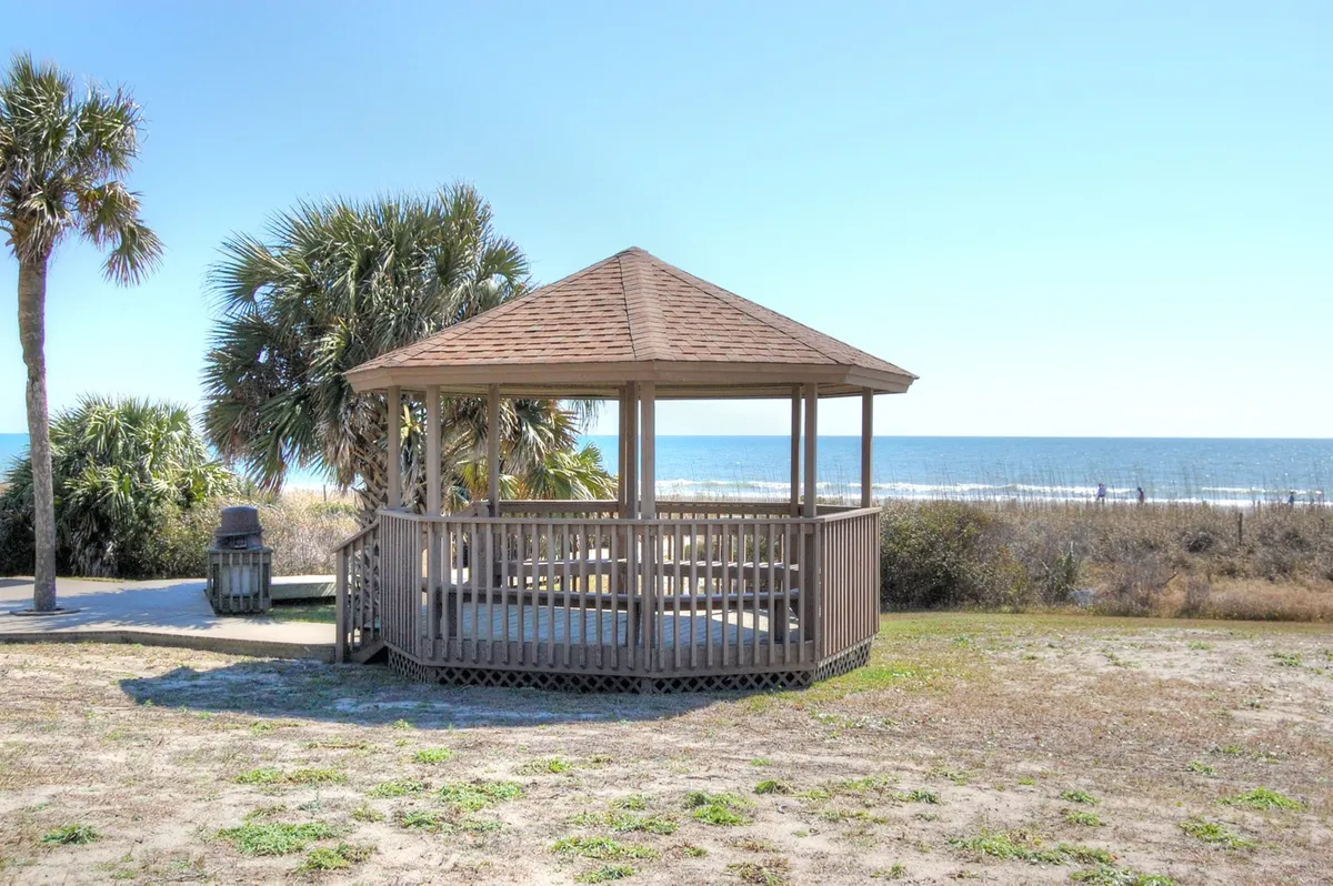 A serene oceanfront view with a gazebo shaded by palm trees overlooking the water. The open green area and calm atmosphere invite relaxation, outdoor gatherings, and nature appreciation—a quintessential coastal retreat setting.