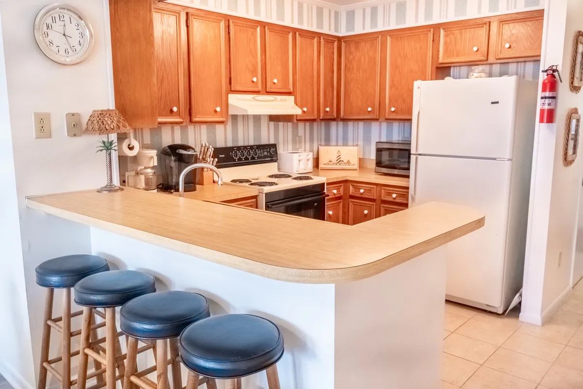 A modern, fully equipped kitchen with a central island, bar stools, wooden cabinets, and sleek appliances. The island encourages casual conversation and provides a spot for meal preparation or enjoying a quick breakfast together.