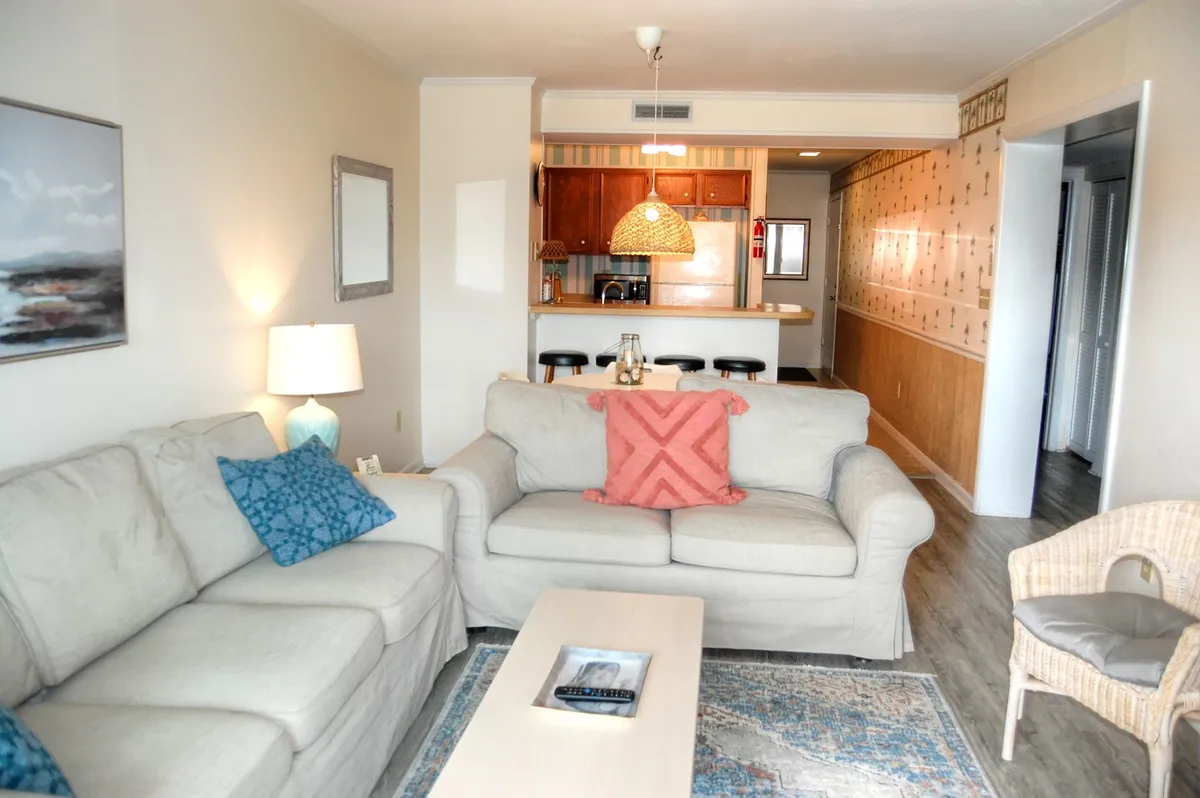 A cozy living space with a comfortable sofa, decorative pillows, a coffee table, and an open view into the adjacent kitchen. The arrangement suggests a comfortable, climate-controlled setting ideal for relaxing with family or friends.